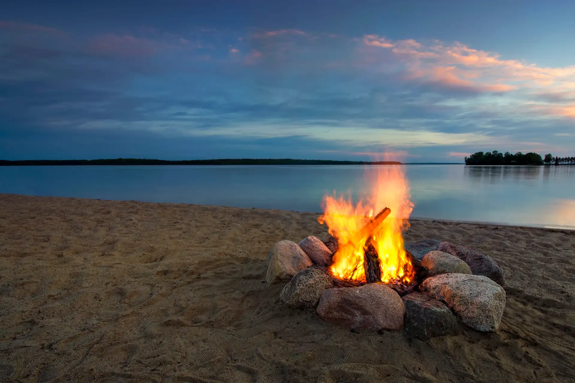 A campfire by a calm lake at dusk.