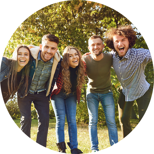 A group of young men and women are all standing outside with their arms around one another. They are smiling and laughing, all of them are enjoying life after treatment for addiction at Jasper Grove Recovery