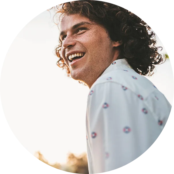 A young man smiles widely while standing outside at sunset. He is enjoying life after addiction treatment at Jasper Grove Recovery.