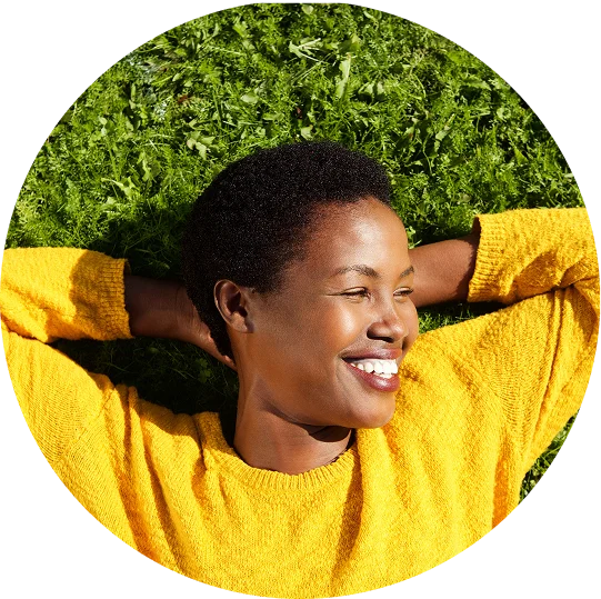 A woman lays in the grass with her hands clasped behind her head. She smiles brightly, enjoying life after addiction treatment at Jasper Grove Recovery.