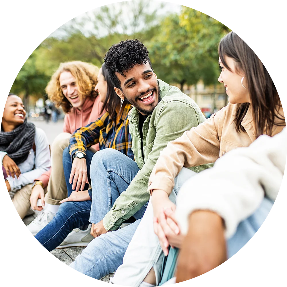 A group of young people, both male and female, are sitting outside. They're smiling, laughing, and enjoying life after addiction treatment at Jasper Grove Recovery.