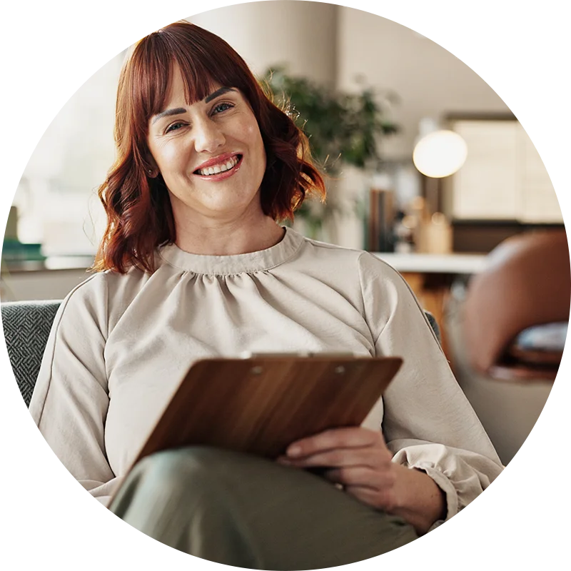 A therapist holding a clipboard, leans back and smiles at her client during an addiction therapy session at Jasper Grove Recovery.