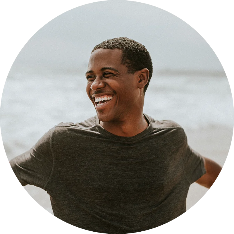 A man, standing lakeside, smiles broadly with his arms stretched wide. He is enjoying life after addiction treatment at Jasper Grove Recovery.